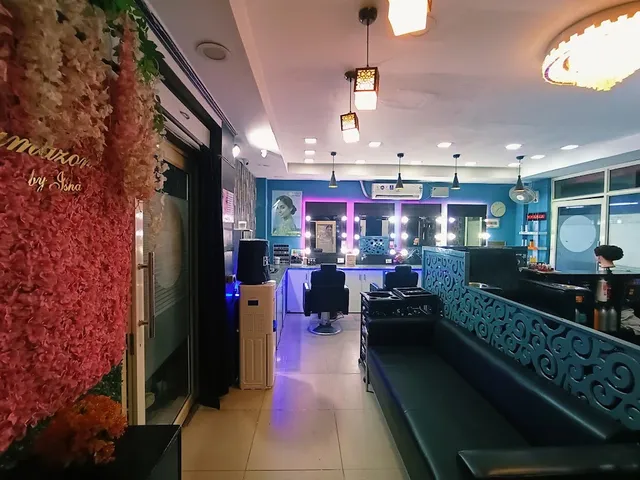 The salon's interior styling floor: a row of mirrors with vanity lighting, styling chairs, a teal accent wall, and "Glamazon by Isha" lettering on a floral display near the entrance.